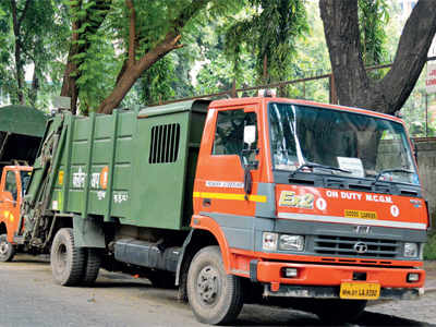 An MCGM refuse compactor truck on duty, parked under trees